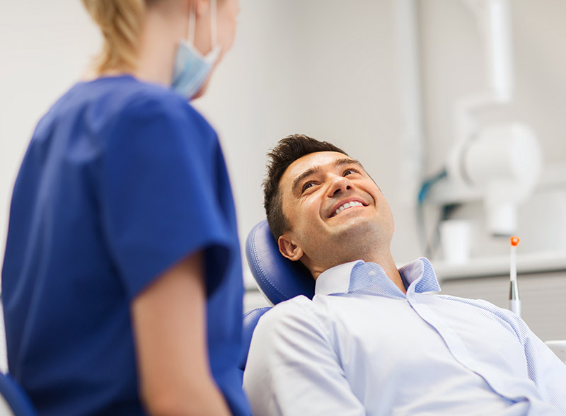man in dental chair smiling at hygienist